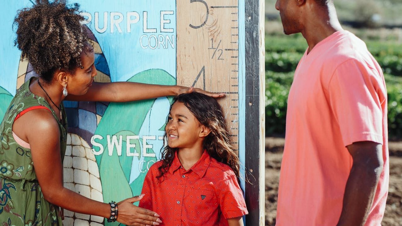 Family measuring a child's height on a wooden marker in a garden.