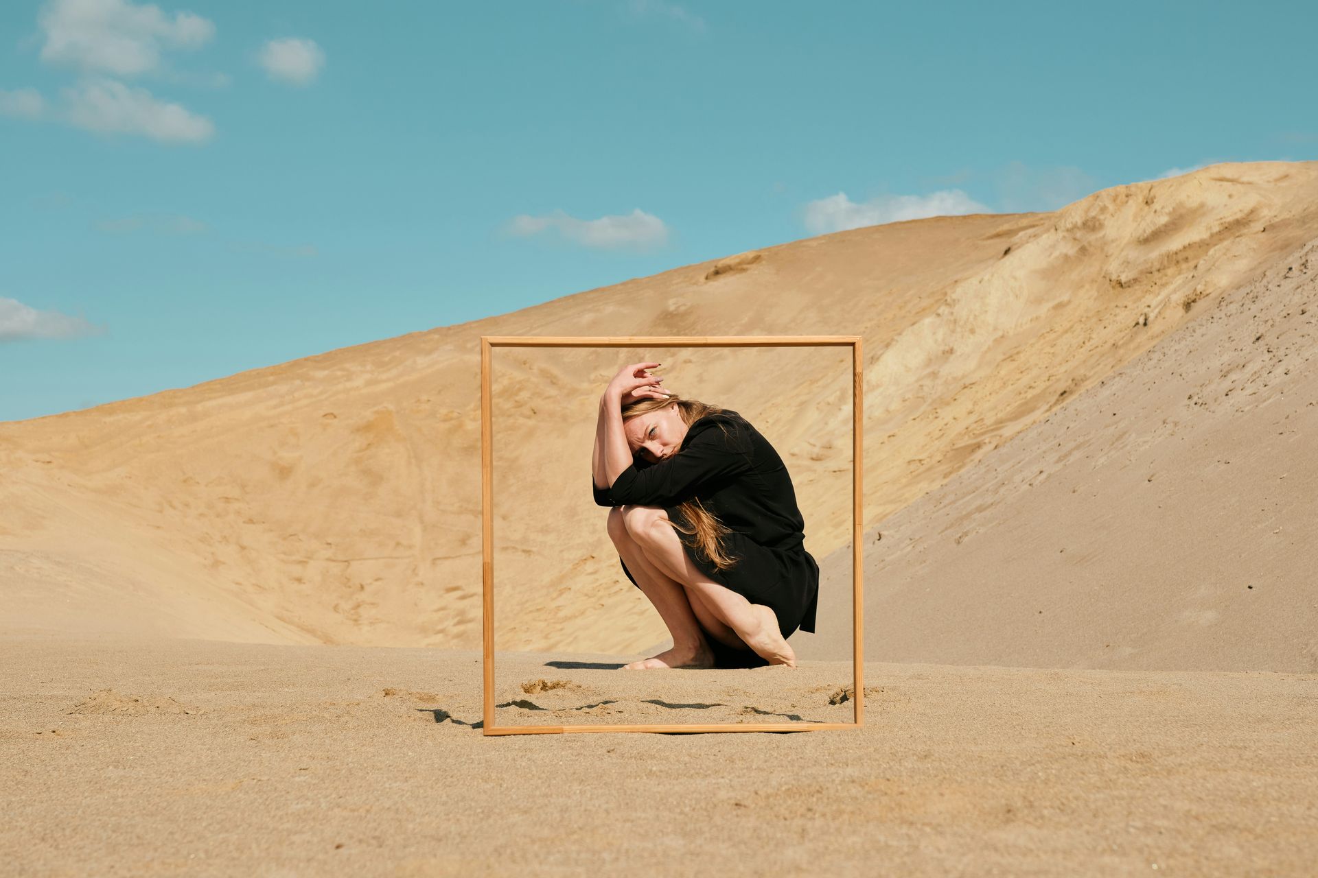 A person kneeling in the sand with a picture frame in front of them