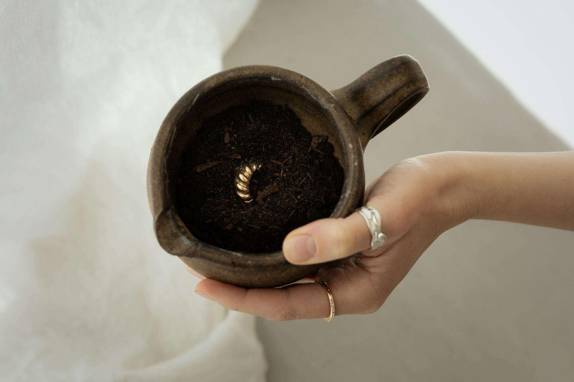 A hand holds a cup containing soil and gold jewelry