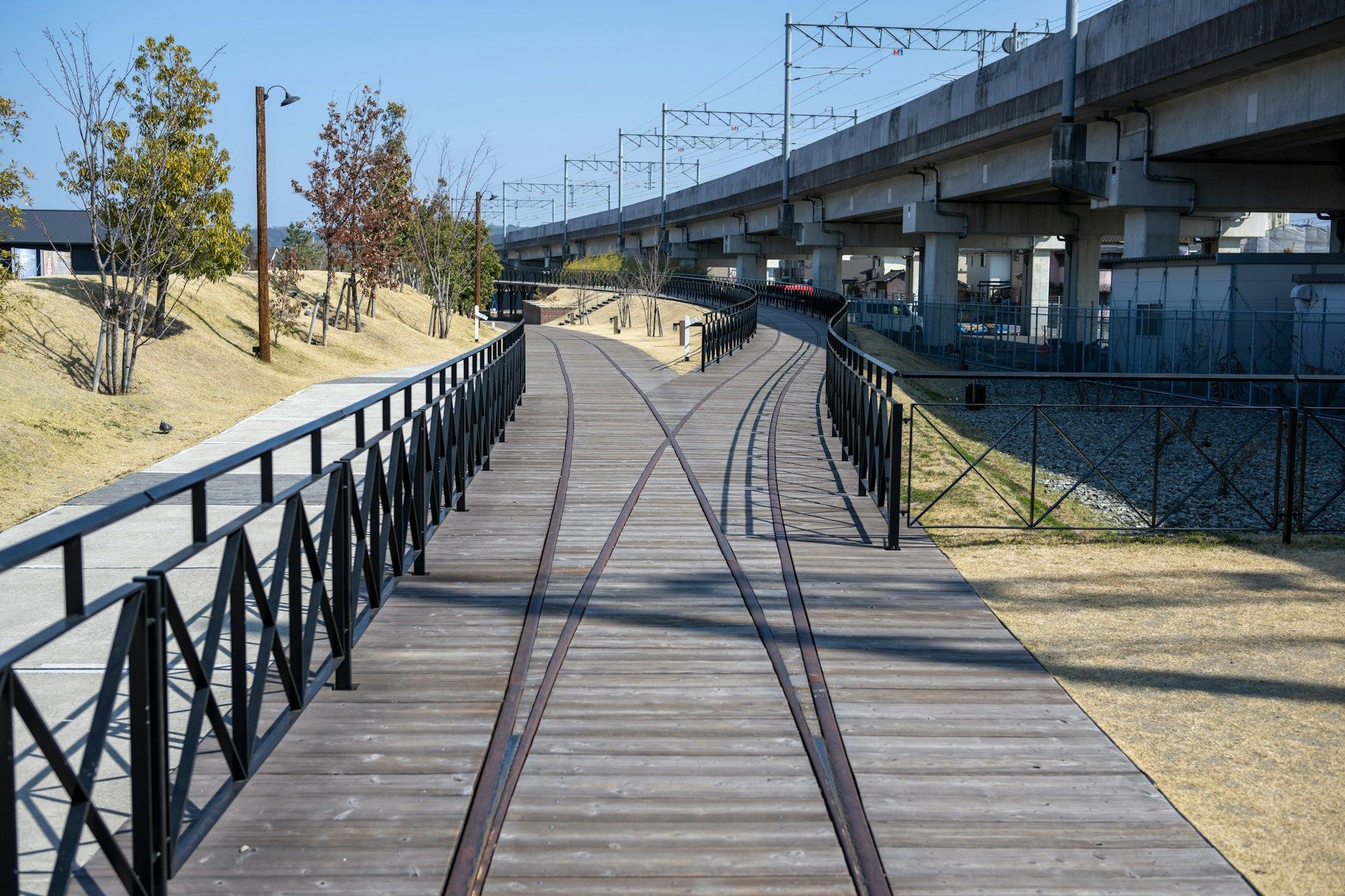 Wooden pathway with train tracks splitting beneath a concrete overpass.