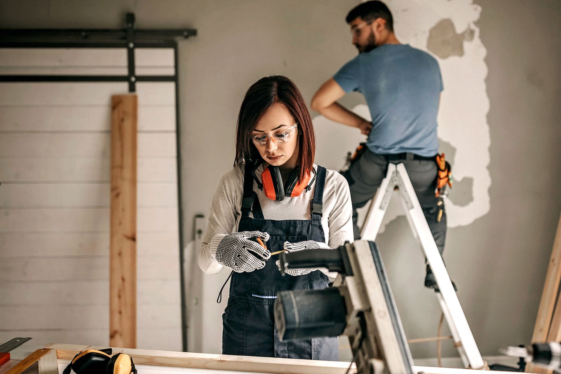 A woman is using a drill in a garage while a man is standing on a ladder — Clifton, NJ — New Alp Construction