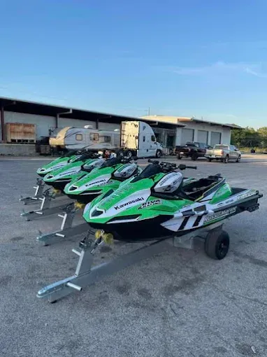 Three green and black Kawasaki Jet Skis on trailers, parked in front of a building.