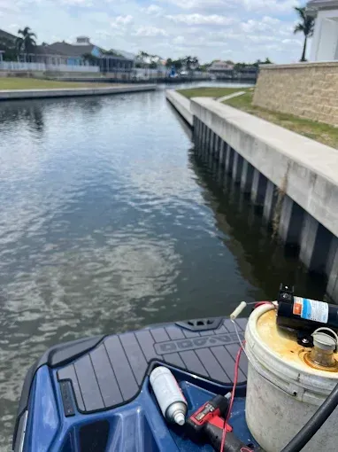 Jet ski in a canal; houses line the sides. Equipment and tools visible on the jet ski.