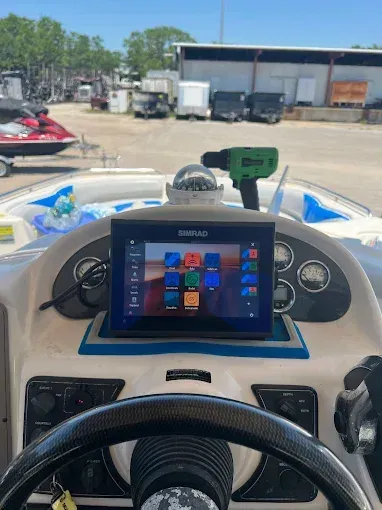 Dashboard of a boat with a Simrad screen, compass, and tools. Bright sunlight, blue and white colors.
