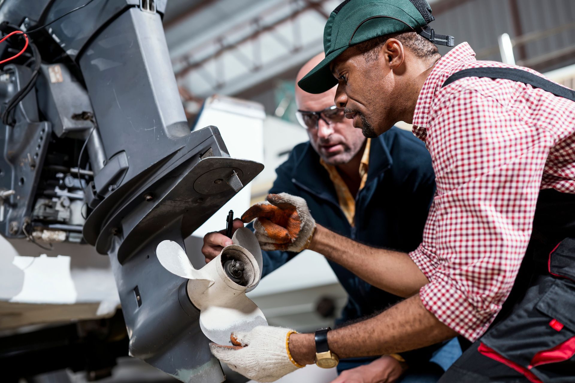 Two people repair a boat’s outboard motor propeller in a workshop.