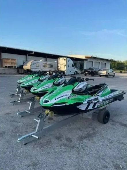 A row of green and white jet skis are parked in a parking lot.