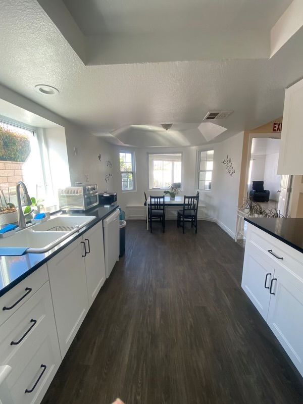Kitchen with white cabinets, dark countertops, a sink, and a dining table.