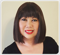 Woman with dark bob and bangs, smiling with red lipstick. Black top, neutral background.