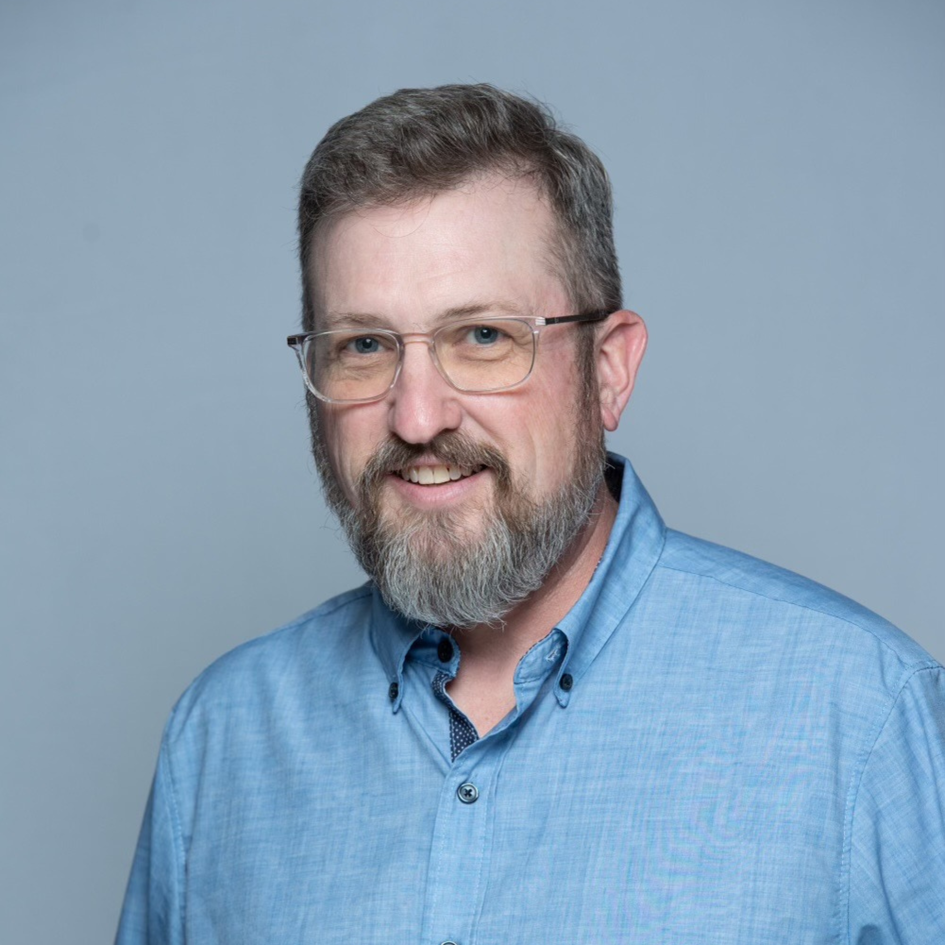 A man with a beard and glasses is wearing a blue shirt.