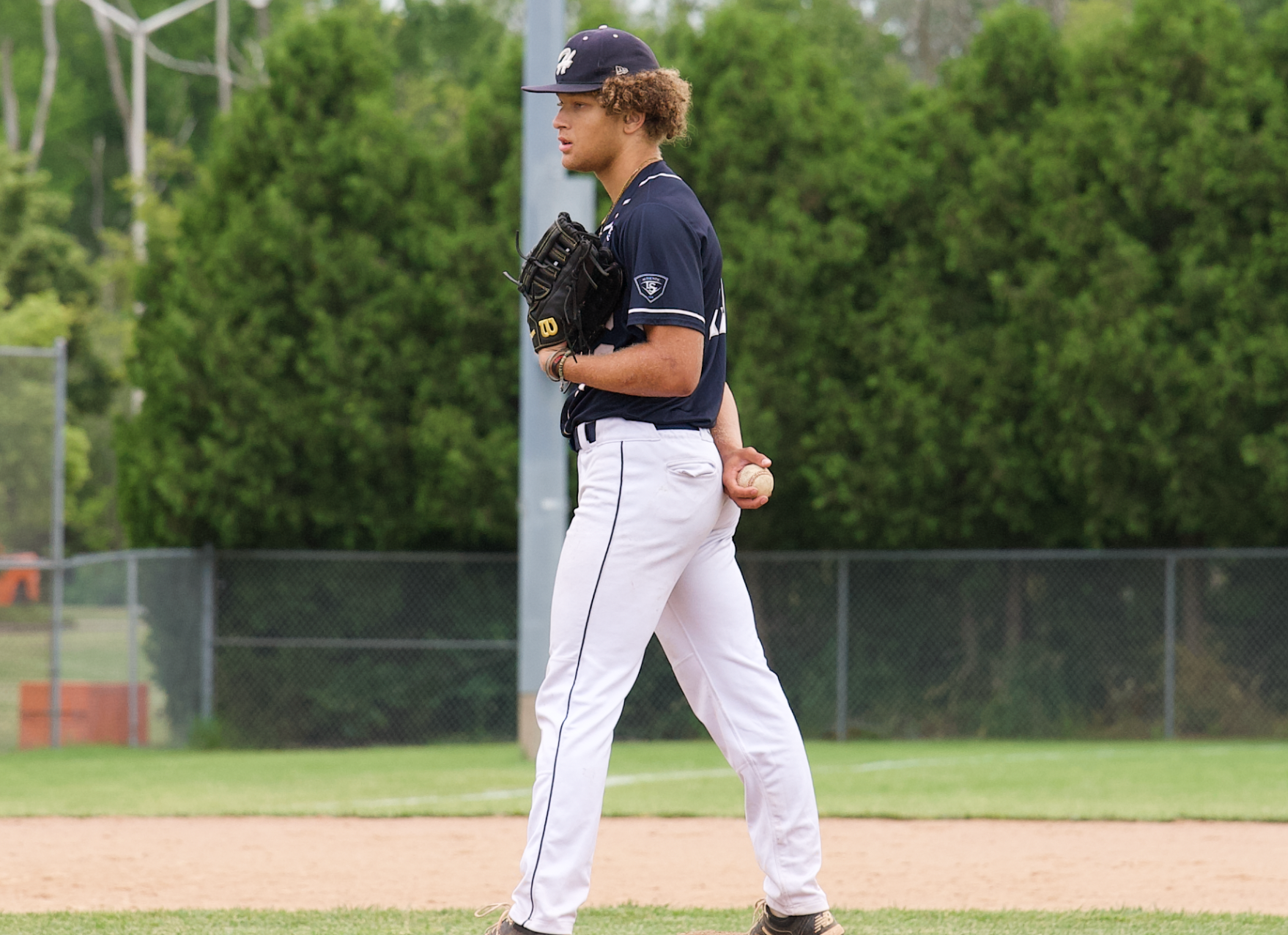 A baseball player is walking on the field holding a ball.