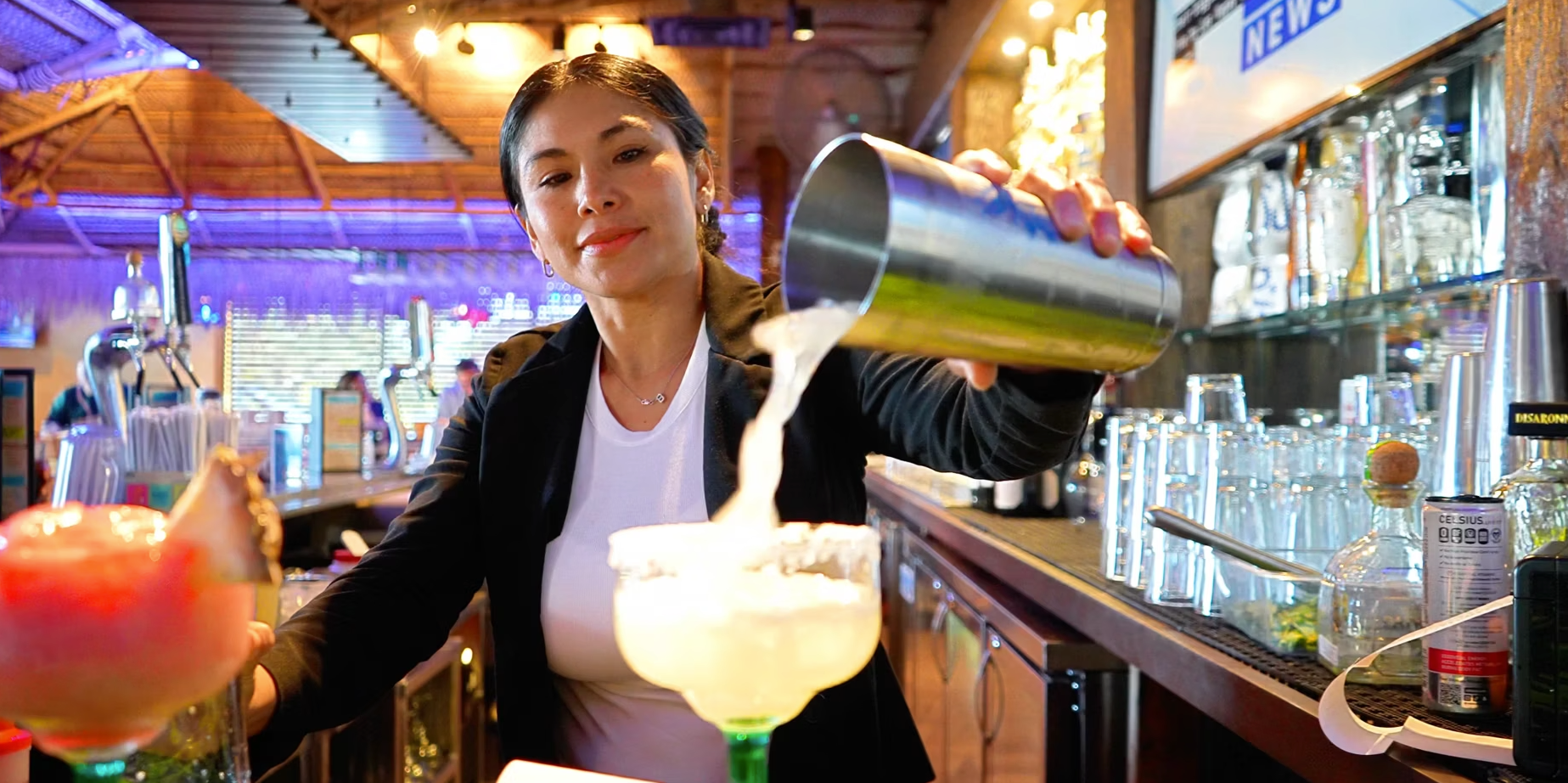 A woman is pouring a drink into a margarita glass at a bar.