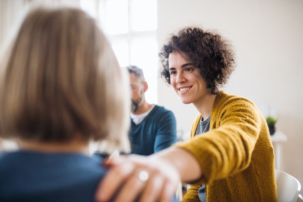 A group of people are sitting around a table talking to each other — Essy K Counselling And Wellness Hub In Croudace Bay NSW