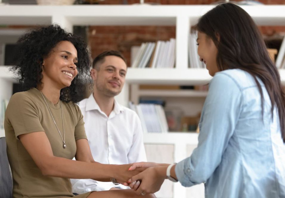 A woman is shaking hands with a man and woman in a living room — Essy K Counselling And Wellness Hub In Croudace Bay NSW