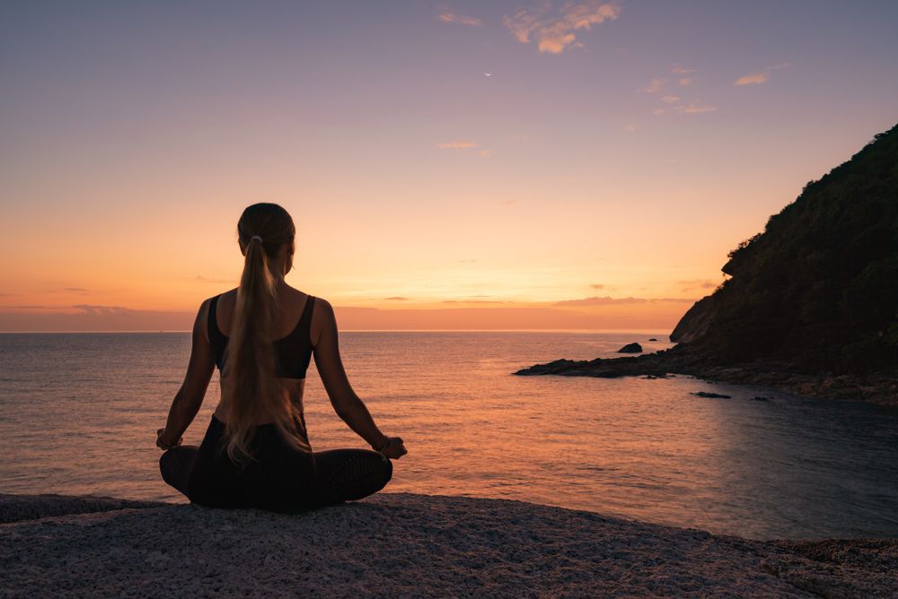 A Woman Is Meditating On The Beach — Essy K Counselling And Wellness Hub In Croudace Bay NSW