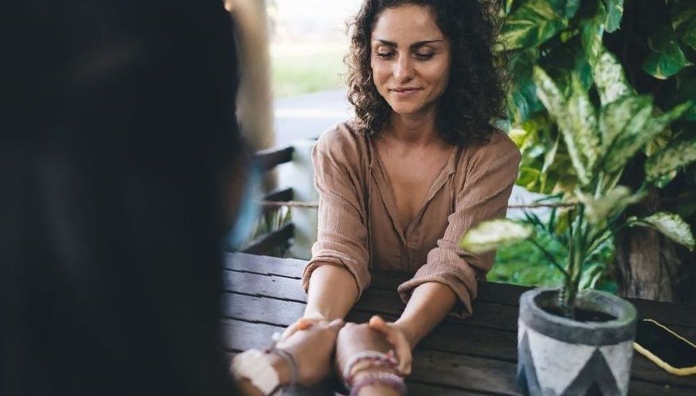 A woman is sitting at a table holding another woman 's hand — Essy K Counselling And Wellness Hub In Croudace Bay NSW