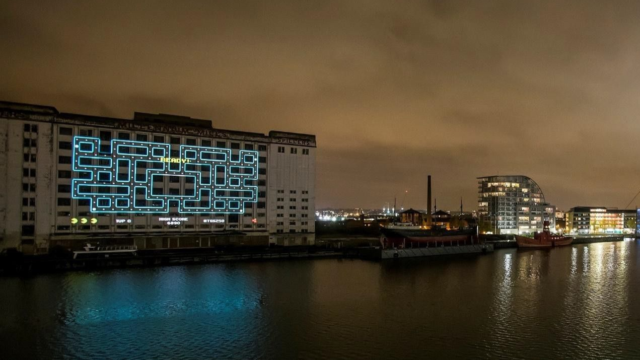 Pac-Man Guiness world record, A building at night with a glowing, blue maze projected on its facade, reflected in the water.