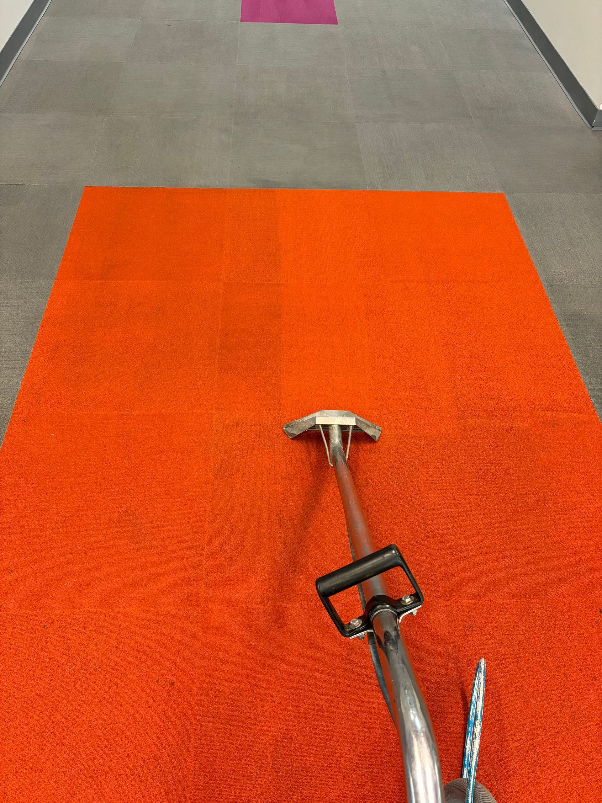 A vacuum cleaner is cleaning an orange carpet in a hallway.