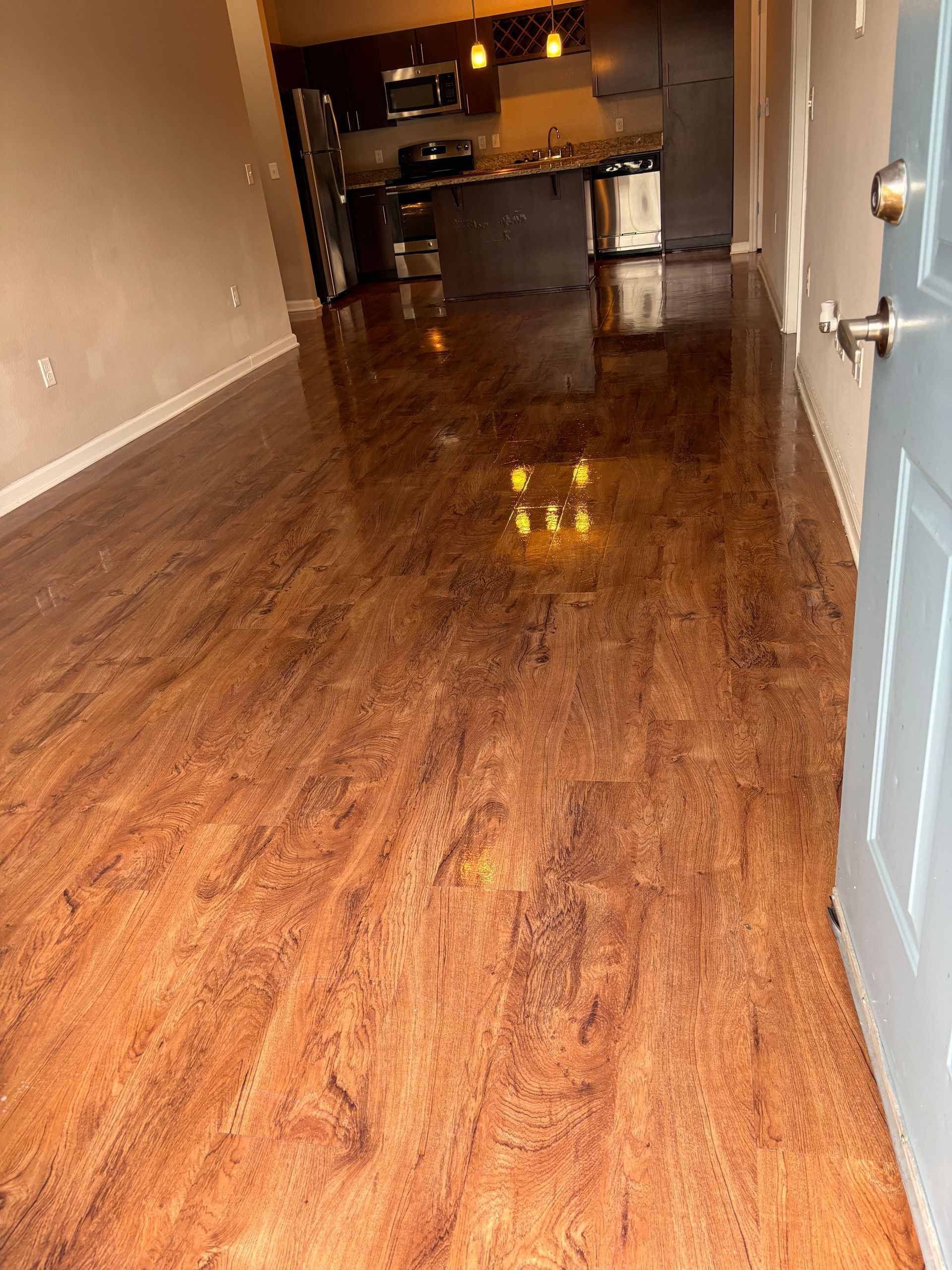 A living room with hardwood floors and a kitchen in the background.