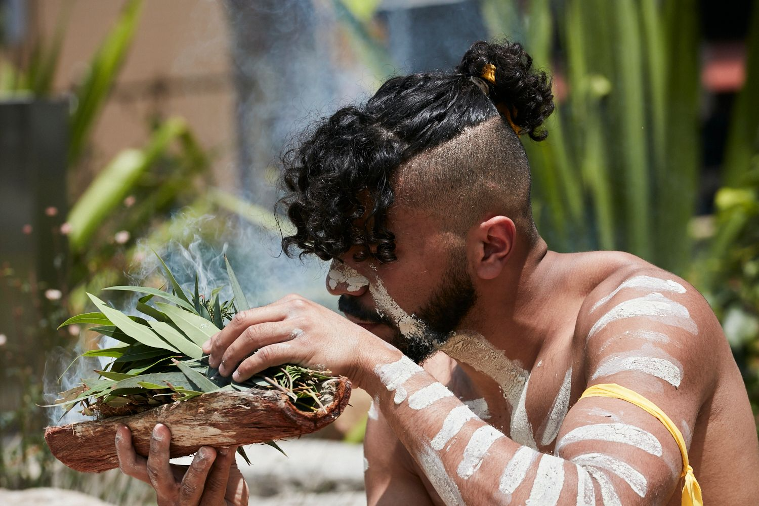 A man with white paint on his arms is holding a pineapple in his hands.