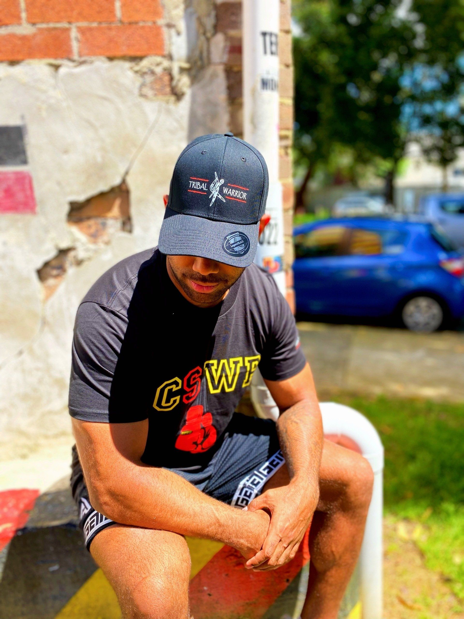 A man wearing a hat and a t-shirt is sitting on a bench.