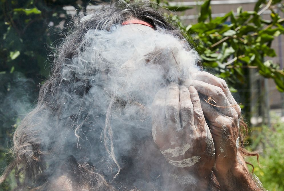 A man with long hair is blowing smoke out of his mouth.