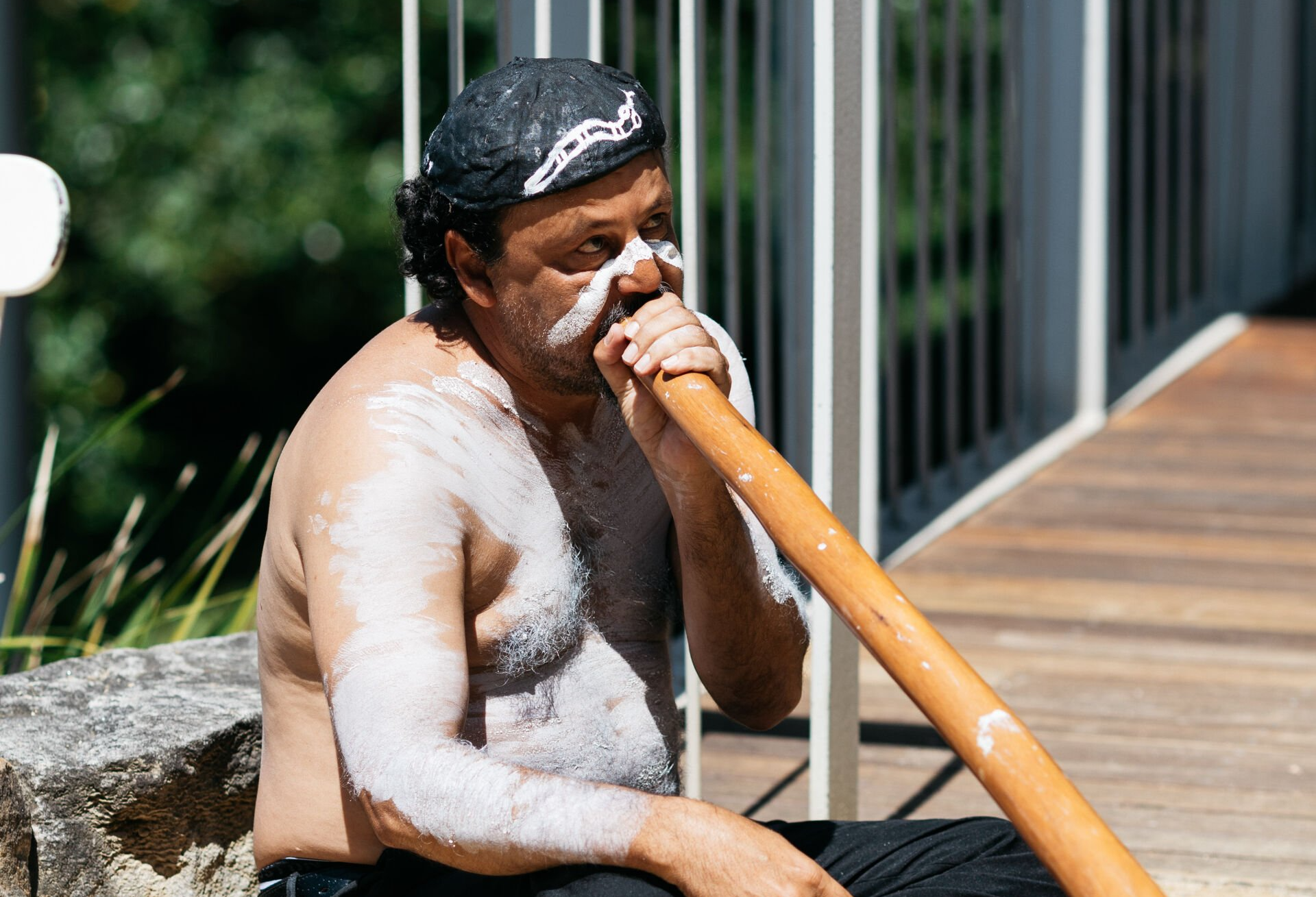 A man with white paint on his face is playing a didgeridoo.