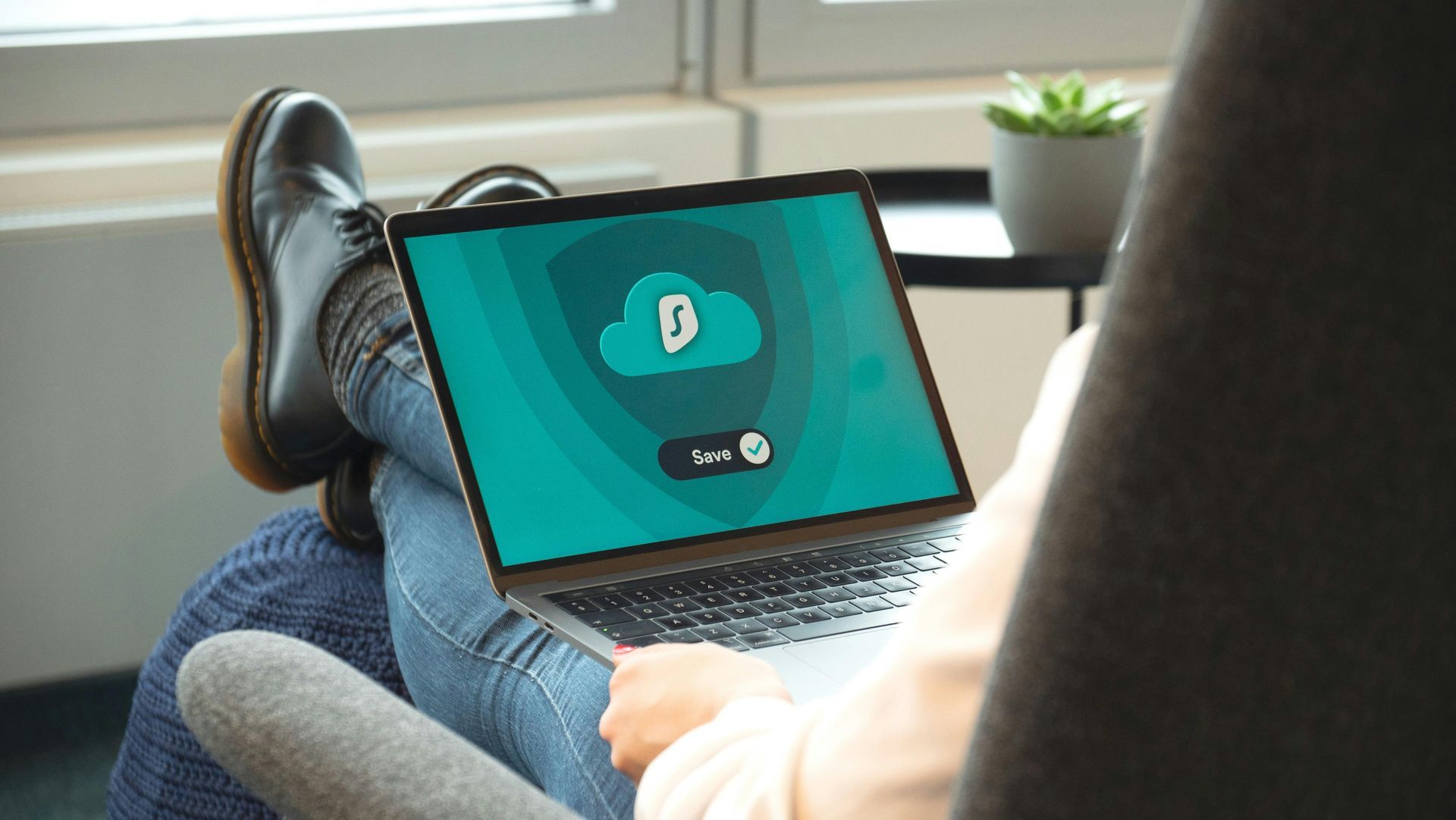 Person sitting with legs crossed, using a laptop with a cloud icon on the screen.