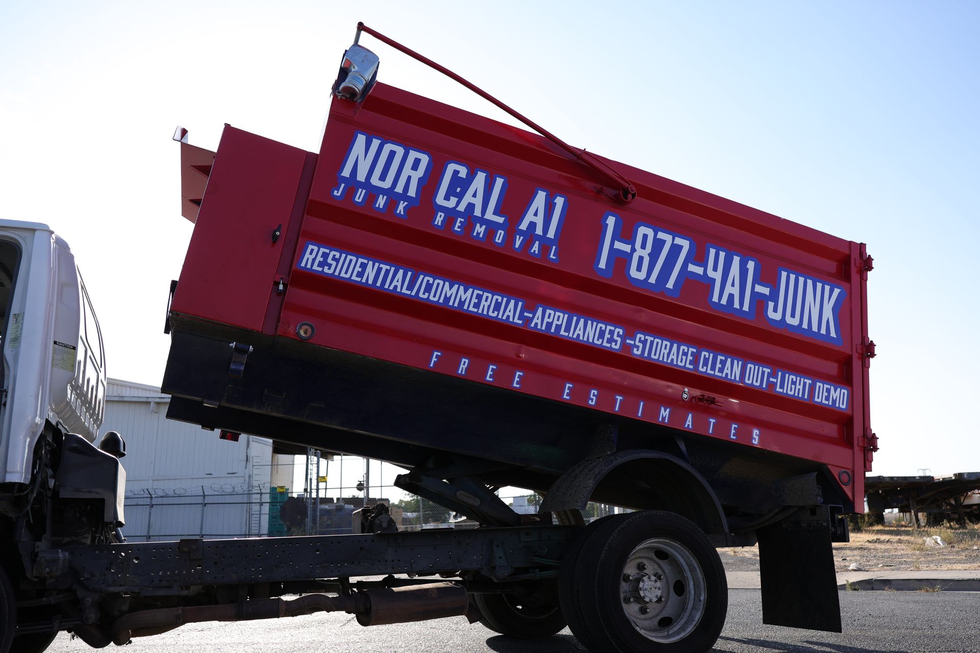 Red NOR CAL AI junk removal truck with tilted bed and phone number.