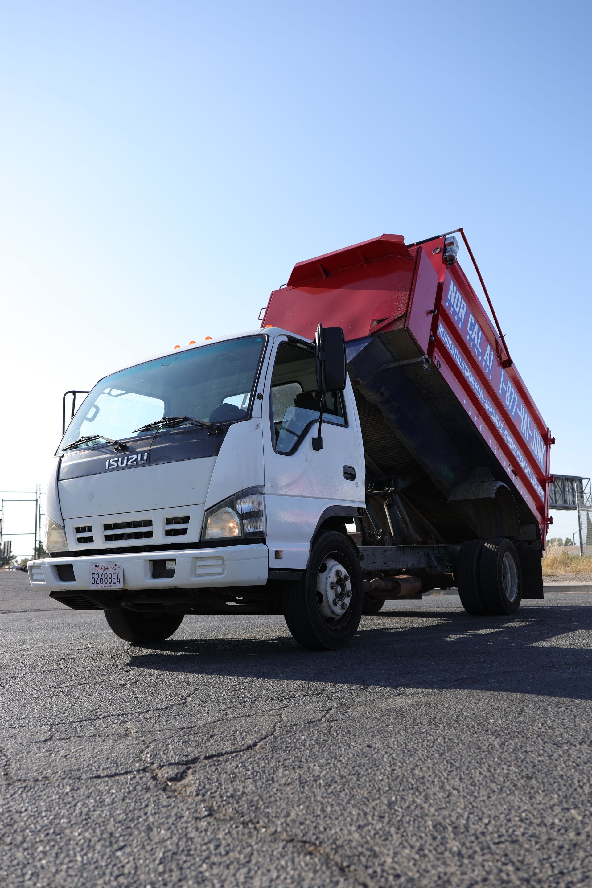 White dump truck with a red bed, parked on gravel under a clear blue sky.