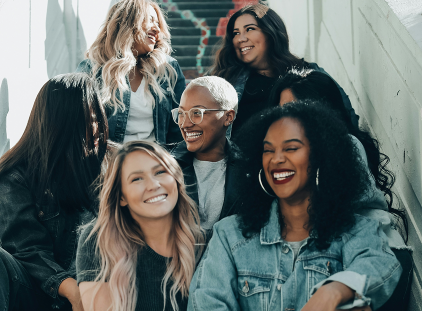 A group of six people smiling and laughing while sitting on outdoor stairs.