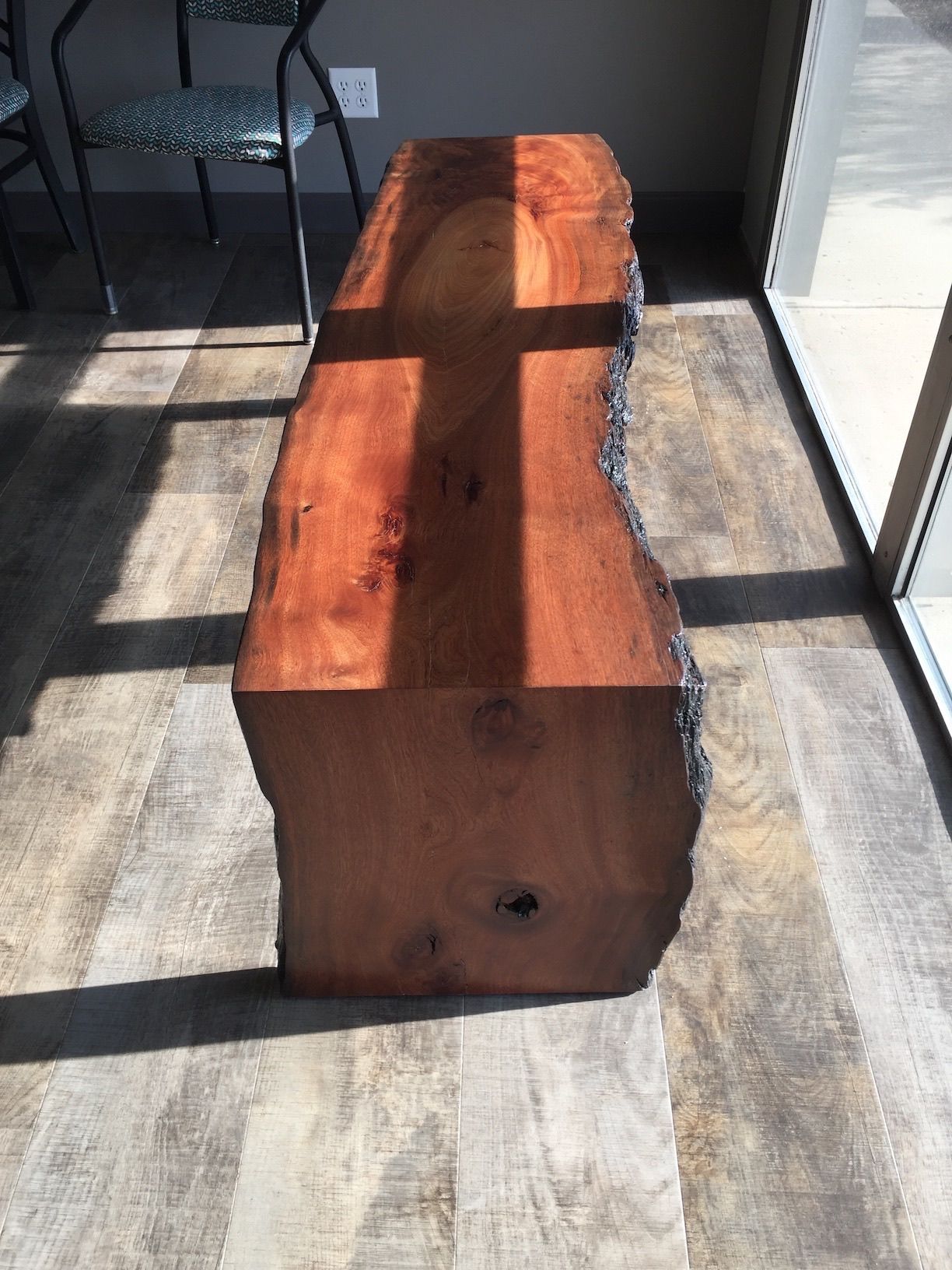A wooden bench is sitting on a wooden floor next to a window.