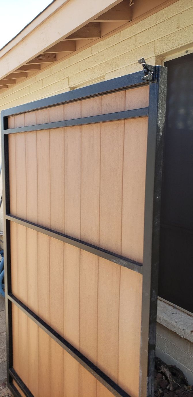 A brown and black metal gate attached to a building, the gate has a wood panel design.