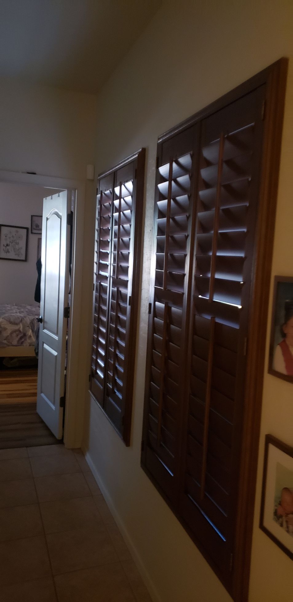 Hallway with dark wooden shutters on the right wall and an open door to a bedroom on the left.