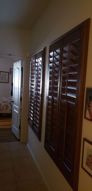 Hallway with brown wooden shutters, white walls, and a door to a bedroom.
