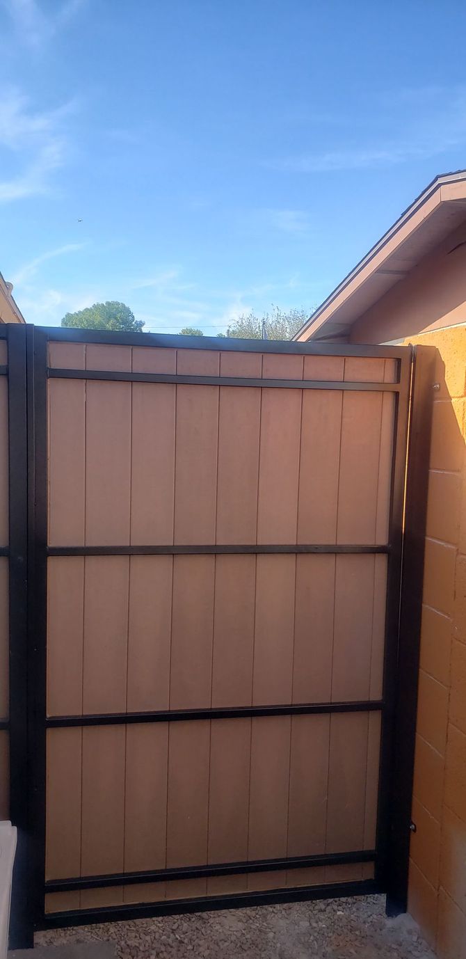 A brown and black fence against a blue sky, partially enclosed by a yellow wall.