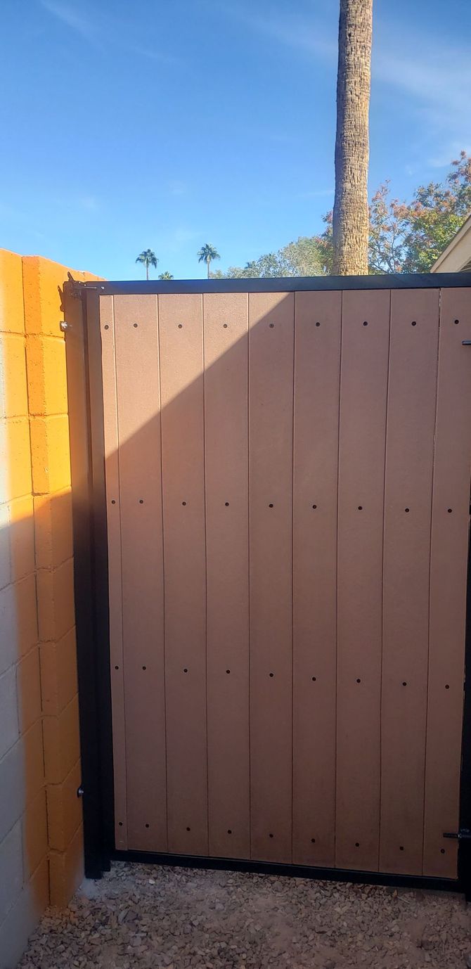 A brown wooden gate in a gravel area with a clear blue sky in the background.