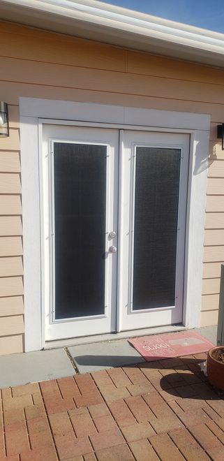 White double doors with dark glass, framed in white, open onto a brick patio.