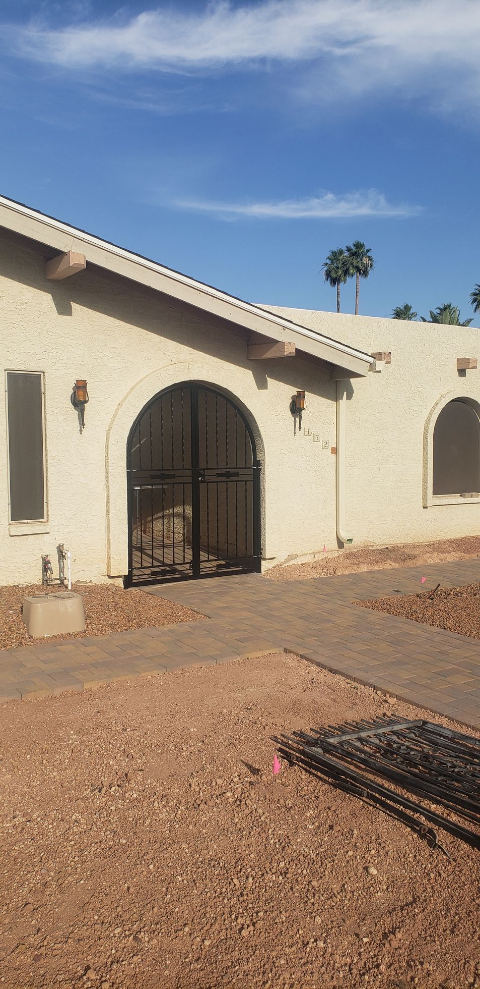 Exterior of a stucco building with a gated archway. Brown gravel and blue sky.