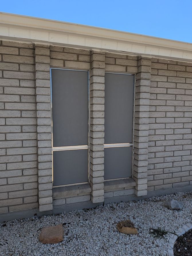 Two tall, narrow windows with gray panels set in a light brick wall, under a white roof.
