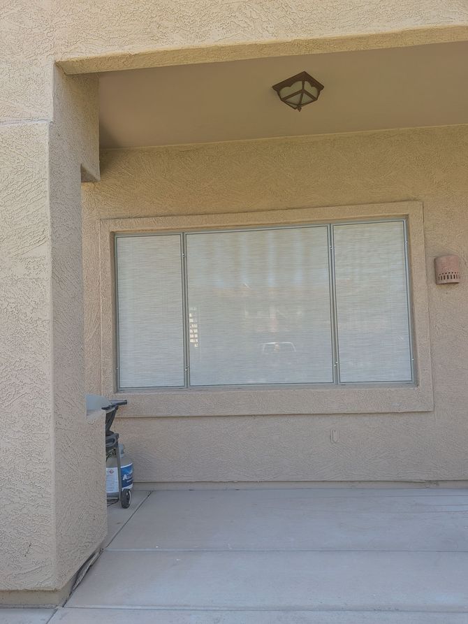 Covered window on a stucco building's porch. A light fixture is mounted above.  A small cart sits beside it.