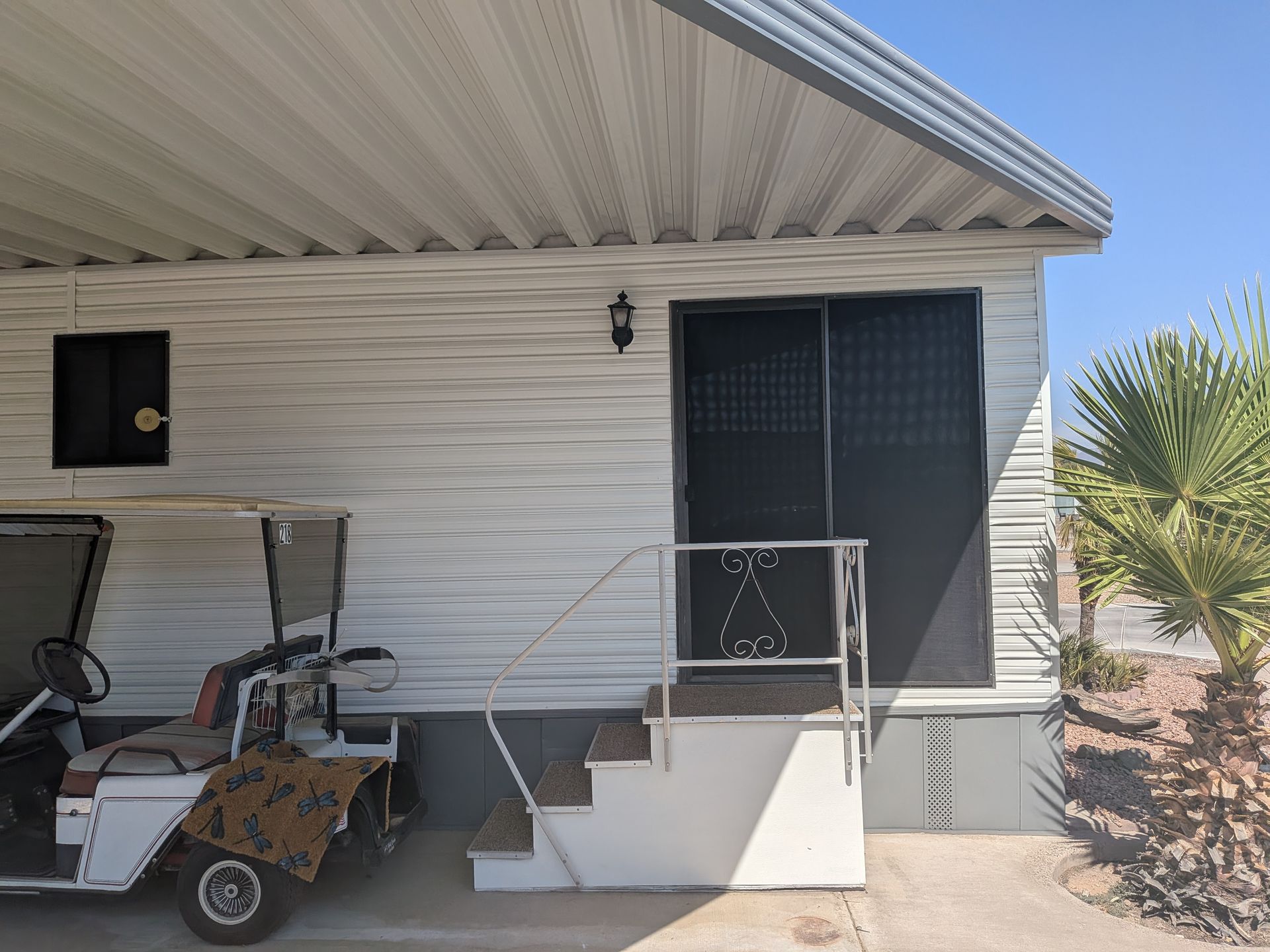 White mobile home with steps, a golf cart, and a screen door.