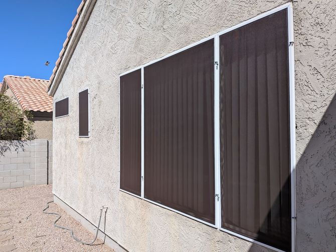 Beige stucco wall with rectangular brown solar screens on windows. White frames.