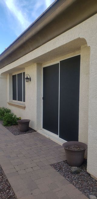 Exterior view of a stucco building with a sliding glass door and a window. A walkway and potted plants are visible.