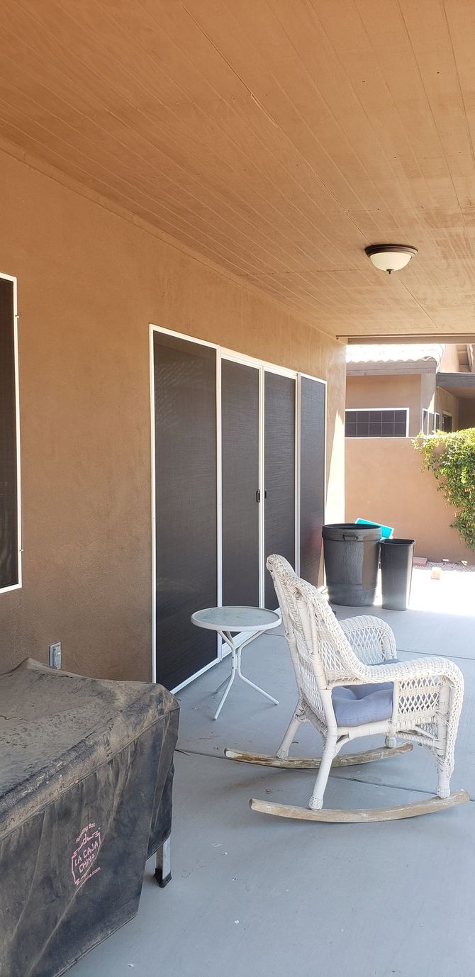 Patio with rocking chair, small table, and covered barbecue grill. Grey and tan color scheme.