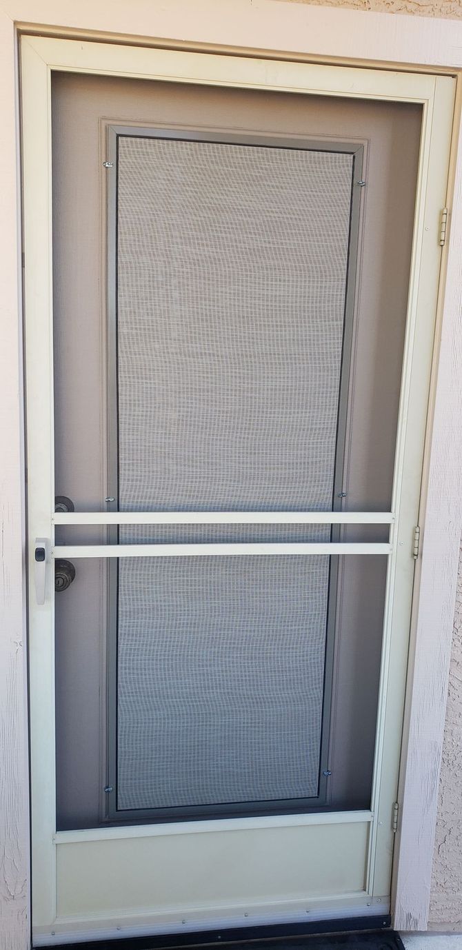 A cream-colored screen door with a horizontal bar across the middle is set against a light-colored wall.