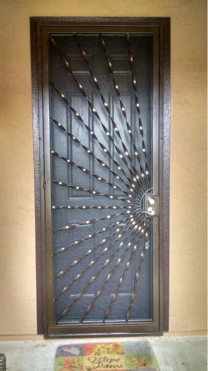 Bronze security door with a radiating spiral pattern, set against a tan wall.