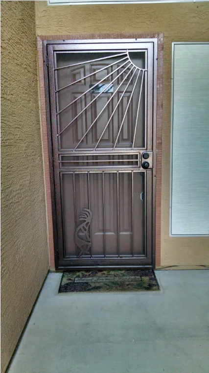 Bronze security door with sunburst design, set in a stucco exterior.