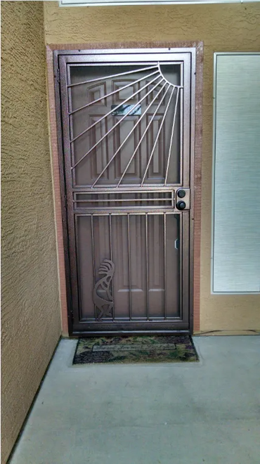 Bronze security door with sunburst design, set in a stucco doorway.