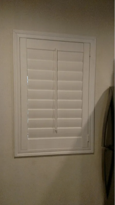 White, closed window shutters in a square frame on a beige wall.