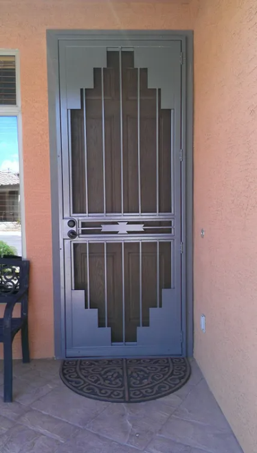Grey metal screen door with diamond design, set in a peach-colored exterior wall. Black mat at the base.